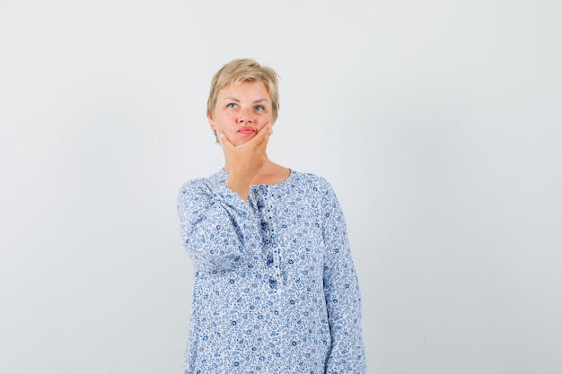 Mature woman holding her chin in dress and looking indecisive.