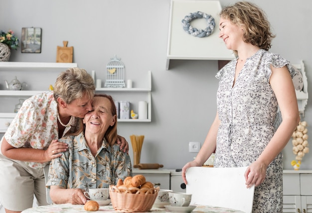 Mature woman kissing her senior mother in kitchen