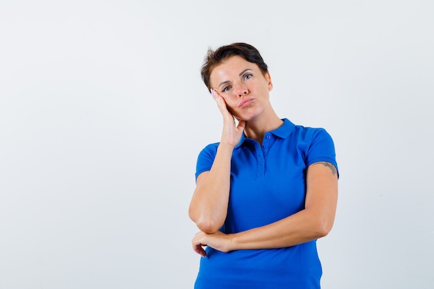 Mature woman leaning cheek on palm in blue t-shirt and looking pensive , front view.