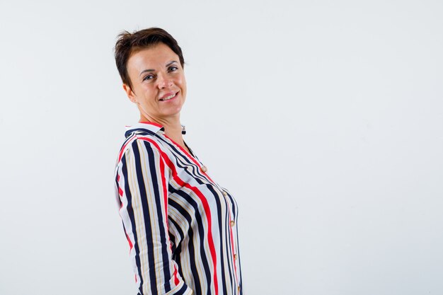 Mature woman looking over shoulder while posing in striped shirt and looking confident. front view.