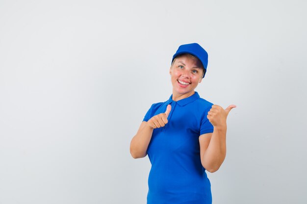 Mature woman pointing aside with thumbs up in blue t-shirt and looking cheery.
