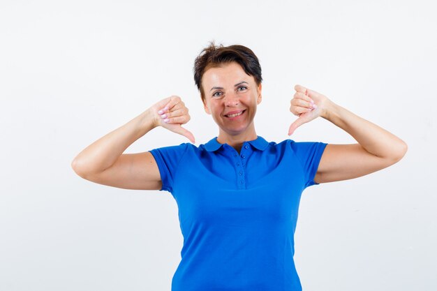 Mature woman pointing at herself with thumbs in blue t-shirt and looking proud. front view.