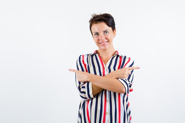 Mature woman pointing at opposite directions, smiling in striped blouse and looking happy , front view.