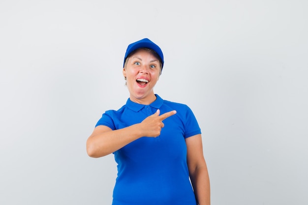 Зрелая женщина, указывая на правую сторону в голубой футболке и выглядя весело.
