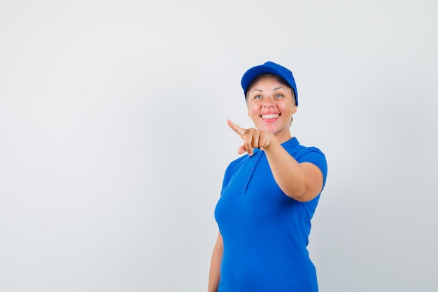 Mature woman pointing at something away in blue t-shirt and looking joyful.