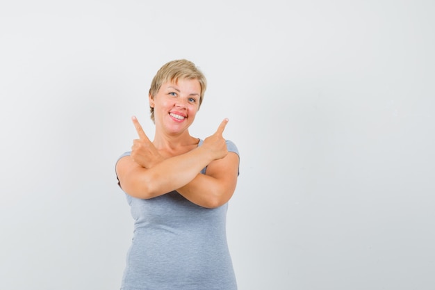 Mature woman pointing up in grey t-shirt and looking cheerful.