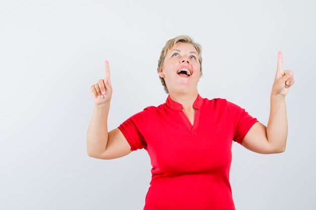 Mature woman pointing up in red t-shirt and looking happy.