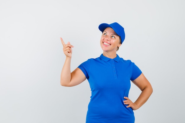 Mature woman pointing at upper left corner in t-shirt and looking hopeful