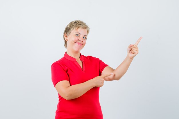 Mature woman pointing at upper right corner in red t-shirt and looking confident