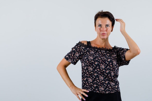 Mature woman posing while keeping hands on waist in blouse and looking attractive , front view.