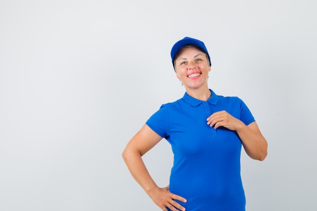 Зрелая женщина позирует с рукой на груди в голубой футболке и выглядит радостной.