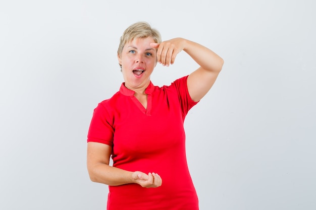 Mature woman pretending to hold or show something in red t-shirt and looking amazed