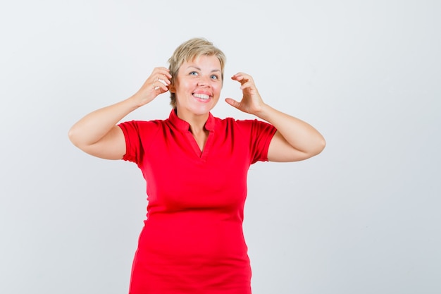 Free photo mature woman pretending to wear headphones in red t-shirt and looking glad