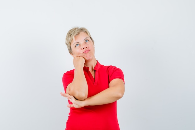 Mature woman propping chin on fist in red t-shirt and looking pensive
