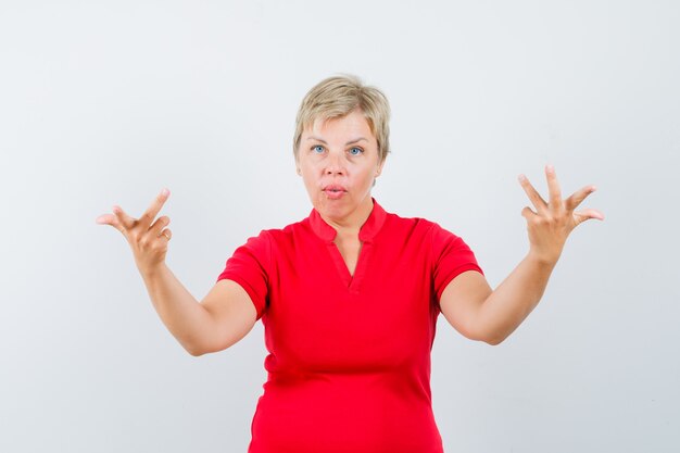 Mature woman raising hands in puzzled gesture in red t-shirt.