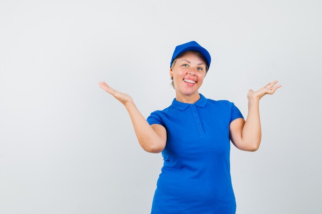 Mature woman raising open palms in blue t-shirt and looking merry.