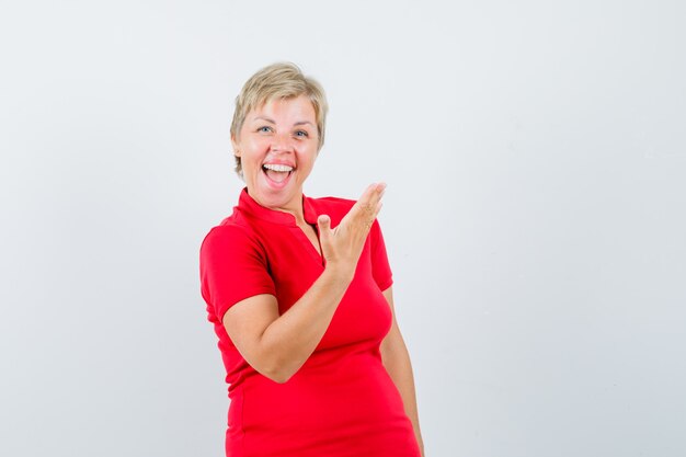 손을 올리는 동안 웃 고 빨간 티셔츠에 성숙한 여자.