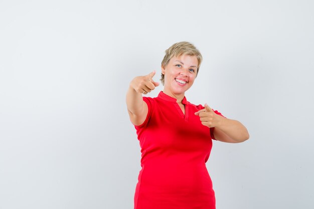 Mature woman in red t-shirt pointing at front and looking confident.