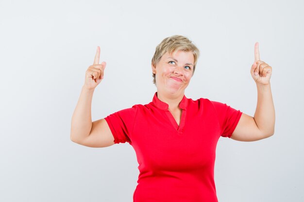 Mature woman in red t-shirt pointing up and looking jolly.