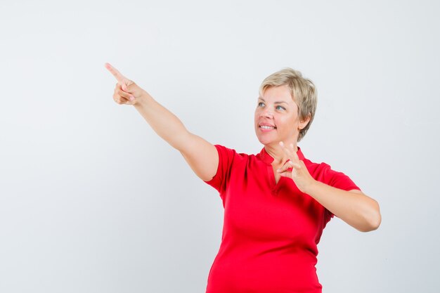 Mature woman in red t-shirt pointing up, showing ok gesture and looking confident.