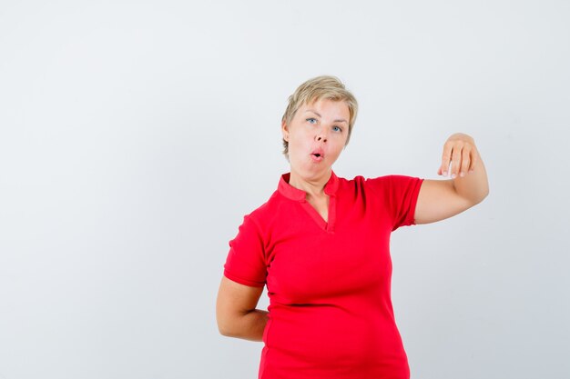 Mature woman in red t-shirt pretending to hold something and looking amazed.