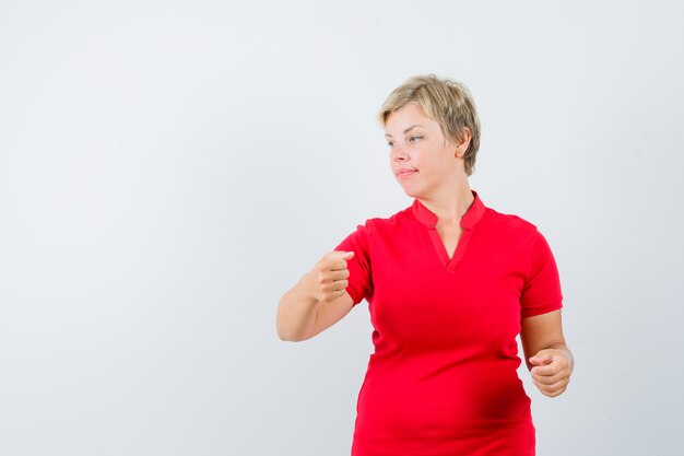 Mature woman in red t-shirt pretending to hold something, looking aside.