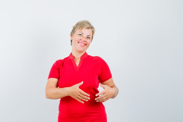 Mature woman in red t-shirt pretending to hold something and looking jolly.