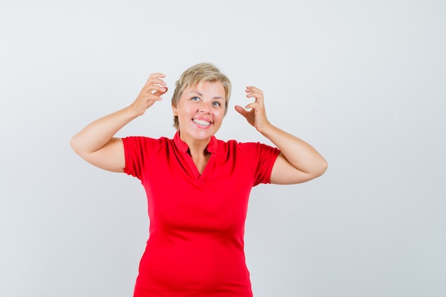 Donna matura in maglietta rossa che finge di togliersi le cuffie e sembra allegra.