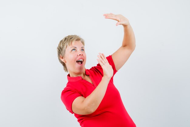 Mature woman in red t-shirt raising hands to defend herself and looking scared