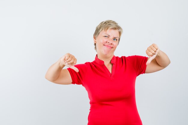 Mature woman in red t-shirt showing double thumbs down and looking dissatisfied