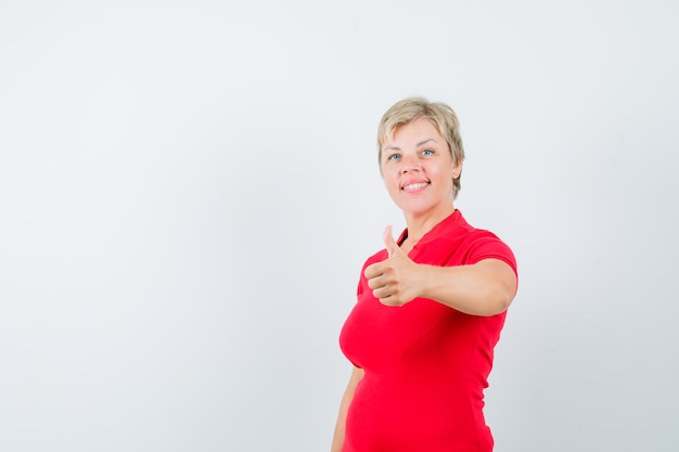 Зрелая женщина в красной футболке показывает палец вверх и выглядит довольной