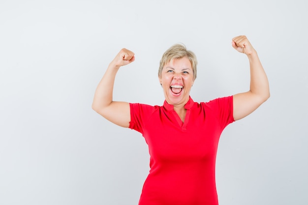 Mature woman in red t-shirt showing winner gesture and looking blissful