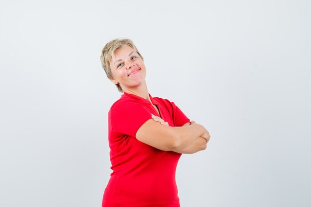 Mature woman in red t-shirt standing with crossed arms and looking proud