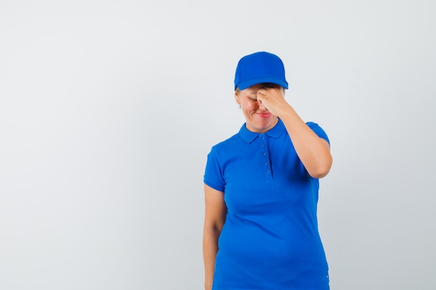 Mature woman rubbing eyes and nose in t-shirt and looking tired.