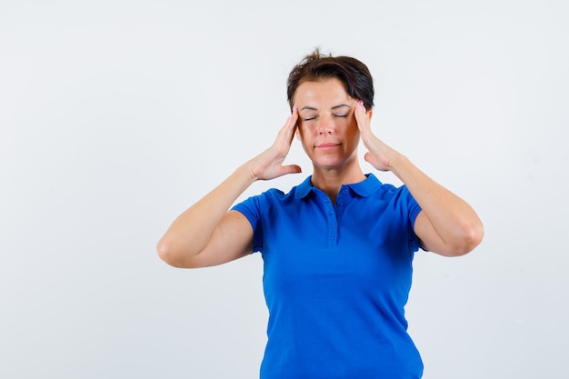 Mature woman rubbing her temples in blue t-shirt and looking relaxed. front view.