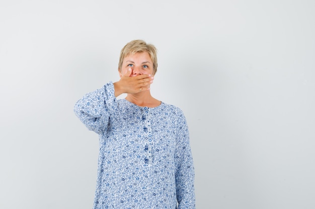 Mature woman in shirt holding hand on mouth and looking mysterious