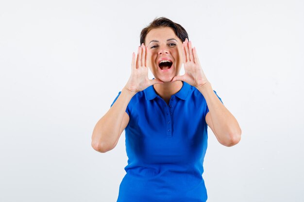 Mature woman shouting or announcing somebody in blue t-shirt and looking excited , front view.