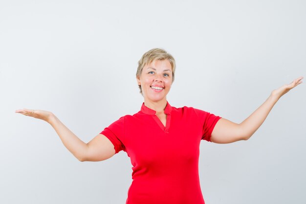 Mature woman showing or comparing something in red t-shirt and looking cheery.