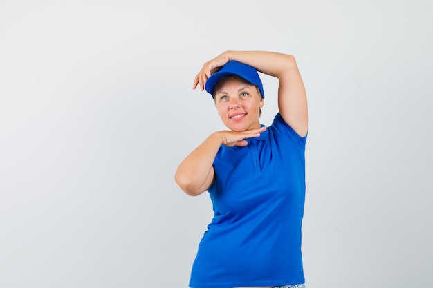 Зрелая женщина показывает жест танца в голубой футболке и выглядит мило.