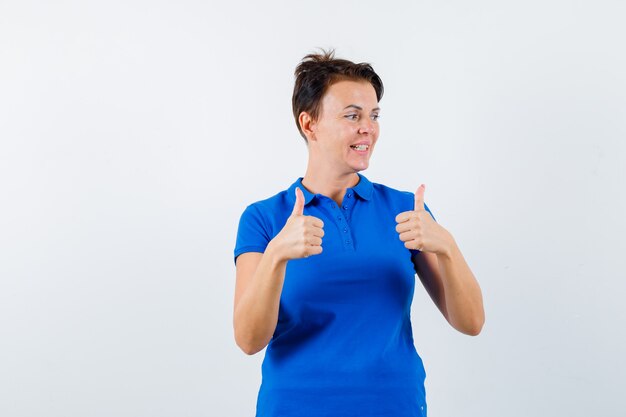 Mature woman showing double thumbs up in blue t-shirt and looking lucky. front view.