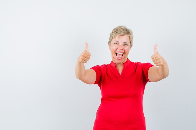 Mature woman showing double thumbs up in red t-shirt and looking lucky.