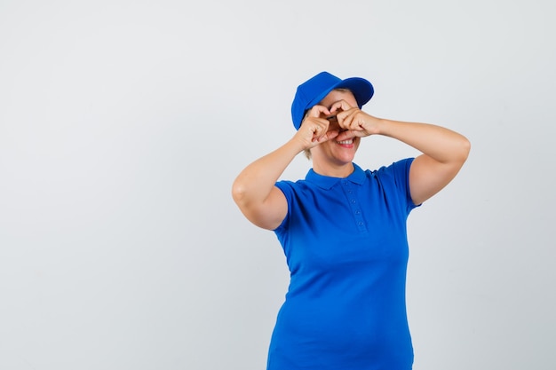 Mature woman showing heart gesture in blue t-shirt and looking glad.