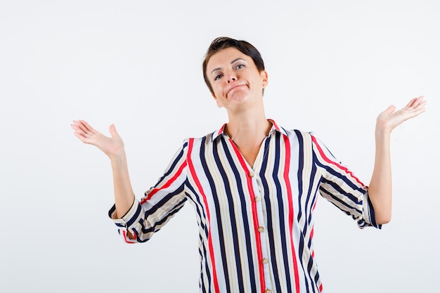 Free photo mature woman showing helpless gesture in striped blouse and looking powerless , front view.