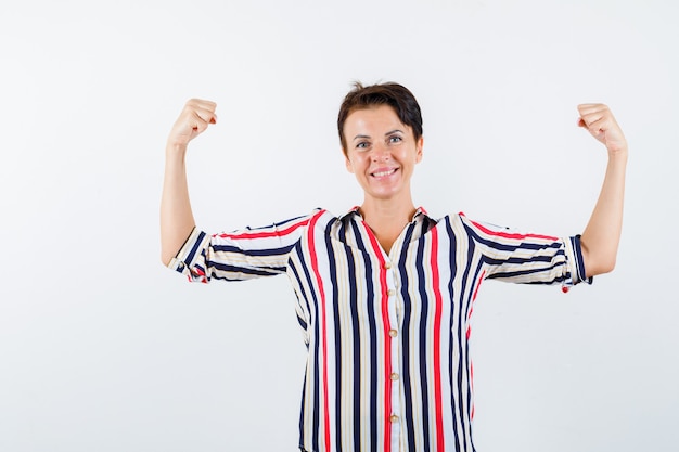 Mature woman showing muscles in striped shirt and looking confident , front view.