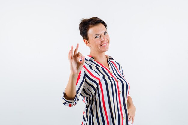 Mature woman showing ok sign in striped blouse and looking buoyant. front view.