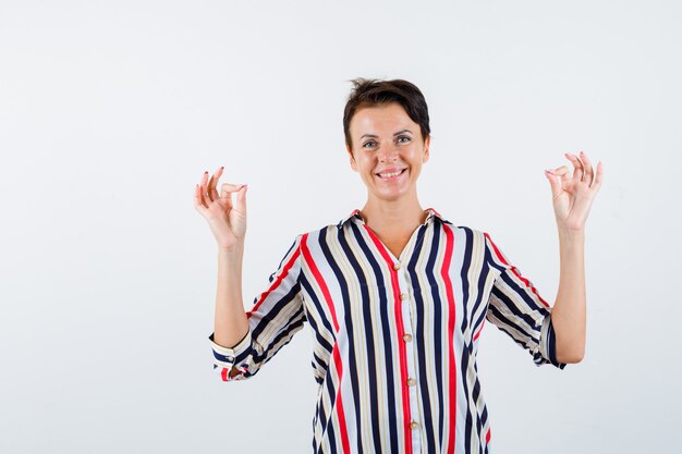 Mature woman showing ok sign in striped blouse and looking buoyant , front view.