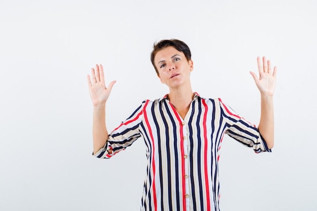 Mature woman showing palms in surrender gesture in striped shirt and looking confident. front view.