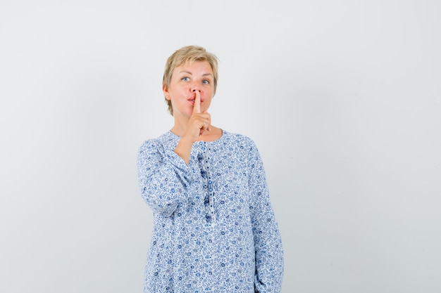 Mature woman showing silence gesture in dress and looking careful.