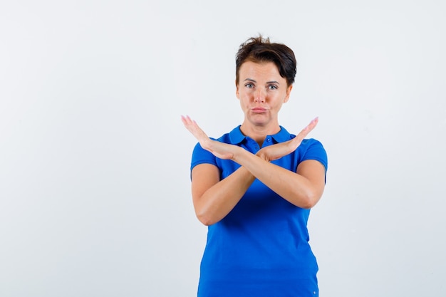 Mature woman showing stop gesture in blue t-shirt and looking disappointed. front view.