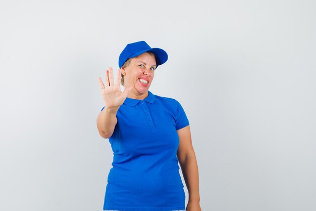 Mature woman showing stop gesture in blue t-shirt and looking funny.